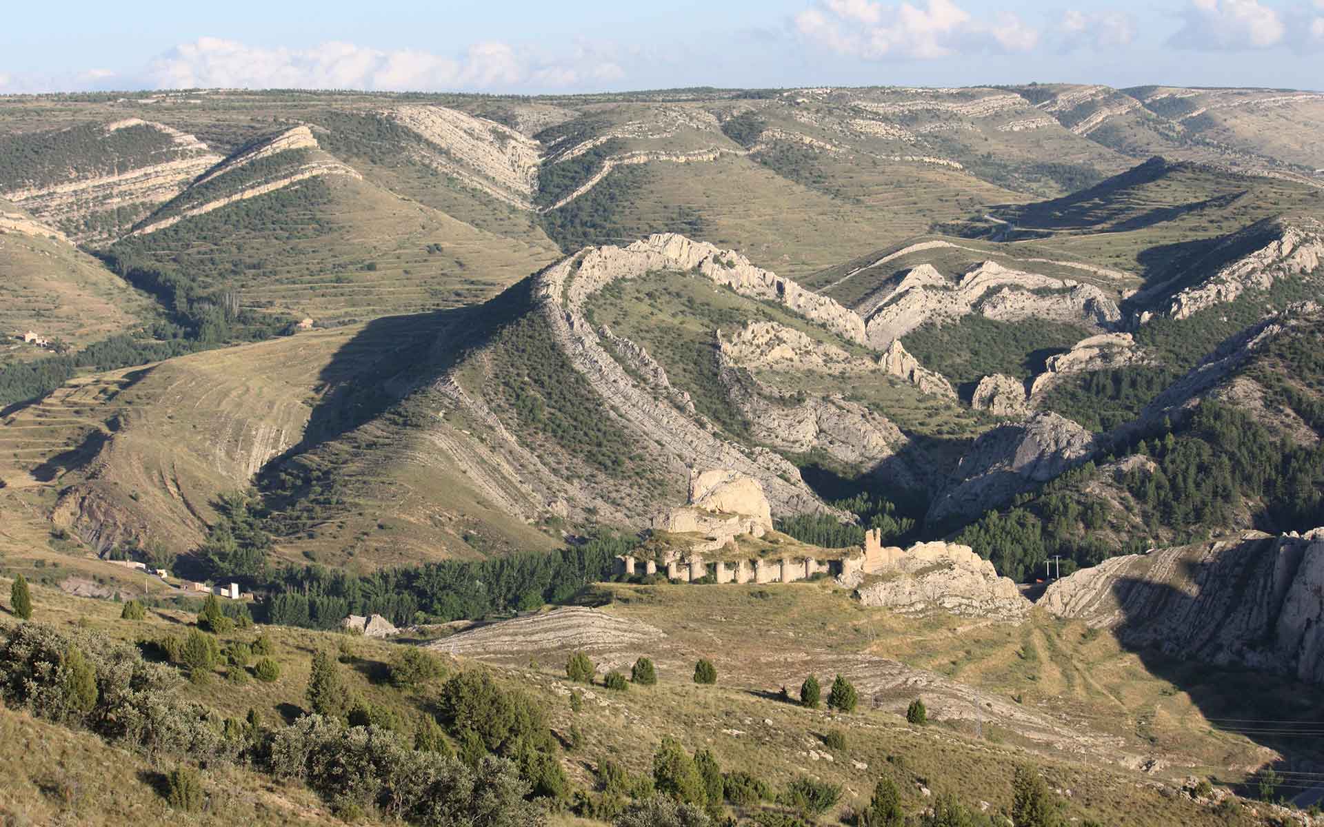 La Olla anticline, second-generation vertical-axis fold affecting Lower Cretaceous marine formations. In front: Aliaga medieval castle. Horizon: Late Neogene planation surface.